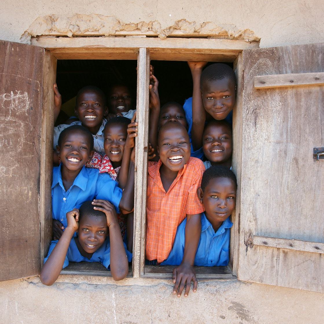 Lachende kinderen leunen samen uit een open raam van een schoolgebouw