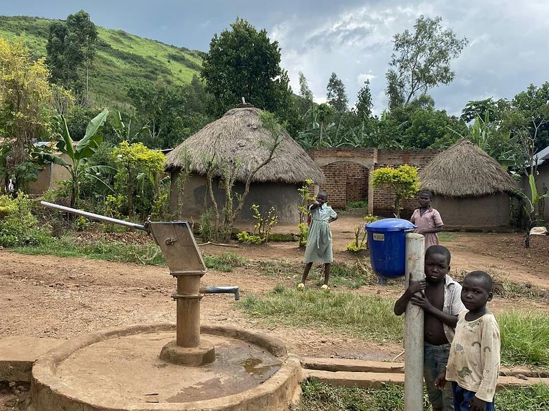 Kinderen bij een waterpomp in een dorp met ronde hutten
