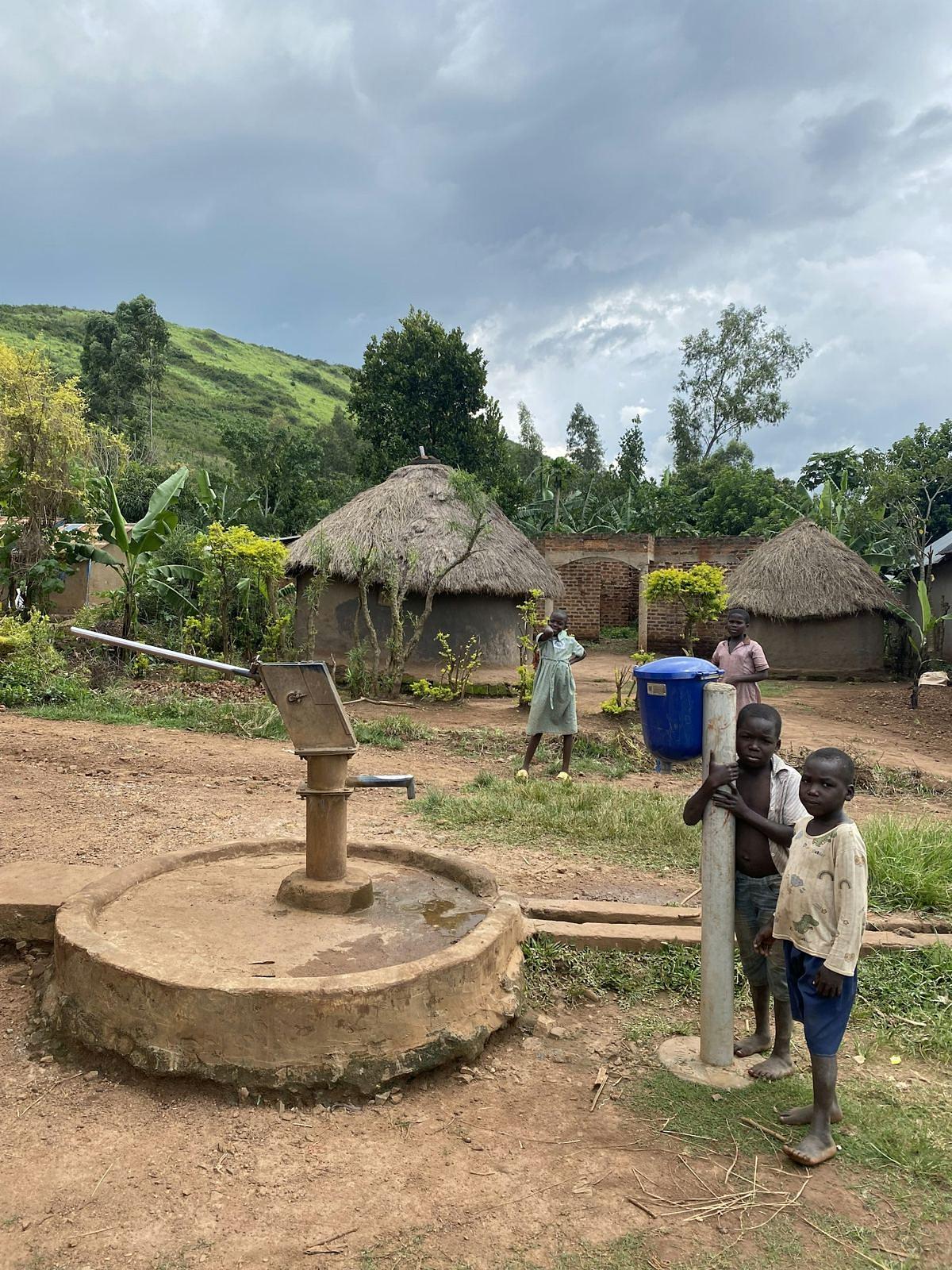 Kinderen bij een waterpomp in een dorp met ronde hutten